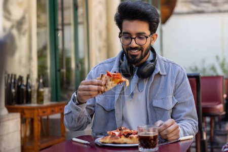 Téléchargez les photos : Pizzeria. Jeune hindou mangeant de la pizza dans la pizzeria - en image libre de droit