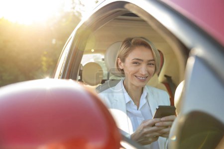 Téléchargez les photos : Jeune femme assise sur le siège avant en voiture et utilisant un téléphone portable - en image libre de droit