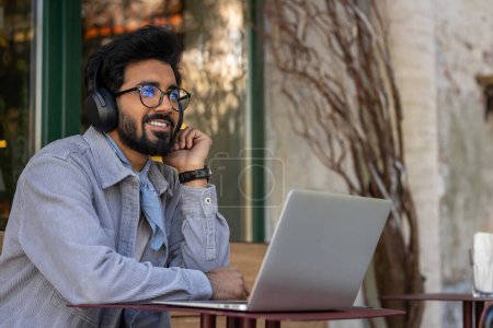 Photo for Good working mood. Hindu man in headphones working on a laptop and looking contented - Royalty Free Image