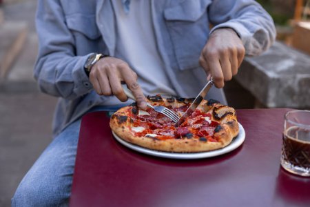 Foto de Pizzería. Hombre sentado a la mesa en un café cortando pizza - Imagen libre de derechos