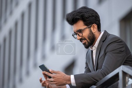 Foto de Sonriendo hombre hindú guapo mensajes de texto en el teléfono y sentirse satisfecho - Imagen libre de derechos