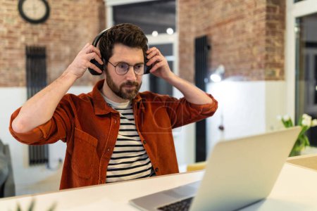 Photo for Young dark-haired man in headphones working on laptop - Royalty Free Image