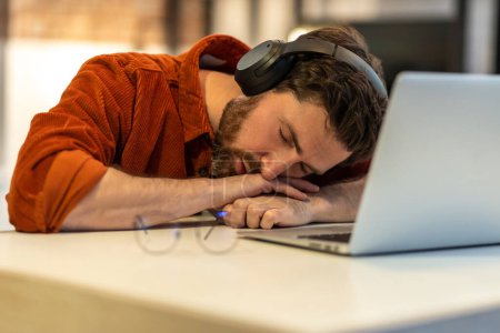 Téléchargez les photos : Homme dans les écouteurs sieste à l'ordinateur portable - en image libre de droit