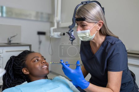 Téléchargez les photos : Une dentiste examine une patiente avec des outils en clinique dentaire qui reçoit un traitement dentaire en clinique - en image libre de droit