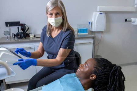 Téléchargez les photos : Femme multiculturelle souriante dans une clinique dentaire faisant un bilan dentaire - en image libre de droit
