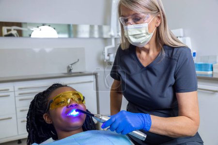 Foto de Mujer dentista haciendo curado dental ajuste de luz resinas compuestas para paciente femenina en clínica - Imagen libre de derechos