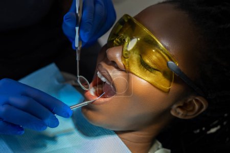 Foto de Dentista irreconocible haciendo procedimiento dental en su consultorio para paciente con gafas protectoras - Imagen libre de derechos