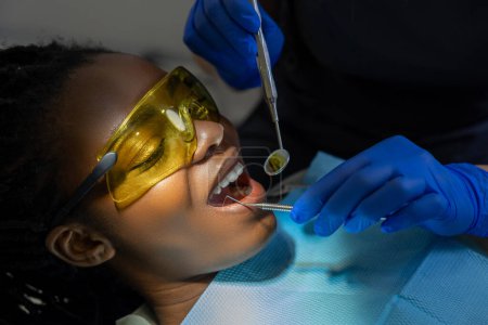 Téléchargez les photos : Patiente multiculturelle dans des lunettes de protection visitant la clinique de stomatologie pour la clinique dentaire - en image libre de droit