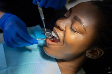 Téléchargez les photos : Dentiste vérifiant les dents de la patiente multiculturelle dans le centre médical moderne - en image libre de droit