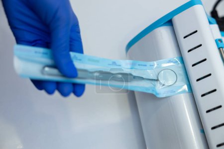 Téléchargez les photos : Mains de dentiste méconnaissables en gants bleus tenant des outils de dentiste à l'aide d'une boîte stérilisante - en image libre de droit
