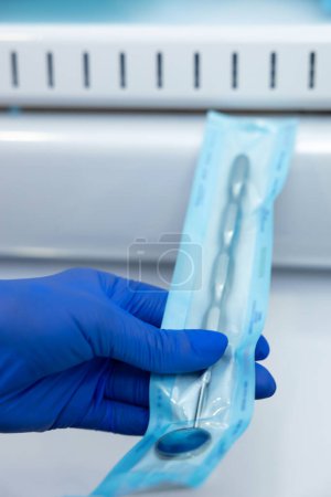 Téléchargez les photos : Mains de dentiste inconnues dans des gants bleus tenant des outils de dentiste effectuant la stérilisation d'instruments - en image libre de droit