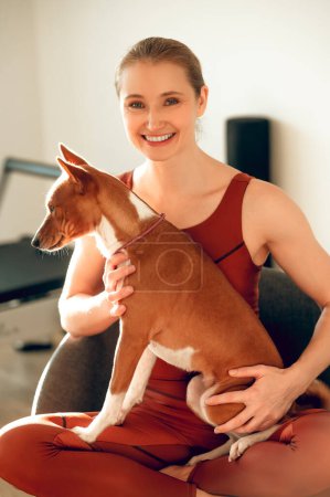Photo for Beautiful sporty woman holding dog in fitness studio - Royalty Free Image