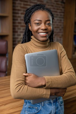 Téléchargez les photos : Femme confiante gaie embrassant ordinateur portable fermé profiter du travail à distance dans le bureau à la maison - en image libre de droit
