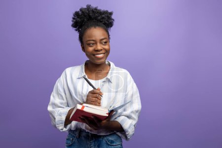 Téléchargez les photos : Jeune femme afro-américaine à la peau foncée en chemise blanche avec un bloc-notes dans les mains - en image libre de droit