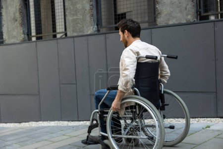 Foto de Incapacidad. Hombre caucásico joven de pelo oscuro montando una silla de ruedas - Imagen libre de derechos