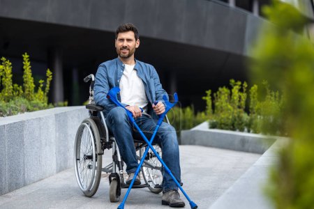 Téléchargez les photos : Invalidité. Jeune homme barbu avec des bâtons sur un fauteuil roulant - en image libre de droit