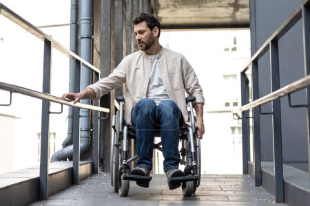 Téléchargez les photos : Invalidité. Brune jeune homme caucasien chevauchant un fauteuil roulant - en image libre de droit