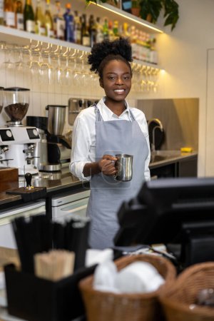 Téléchargez les photos : Femme multiculturelle souriante barista faire du café debout au comptoir dans le café dans le tablier - en image libre de droit