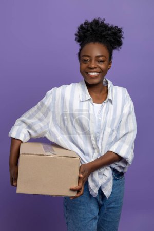 Foto de En el trabajo. Mujer joven de pelo rizado con una caja en la mano sonriendo muy bien - Imagen libre de derechos