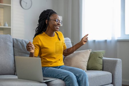 Téléchargez les photos : Jeune femme afro-américaine assise sur le canapé avec ordinateur portable - en image libre de droit