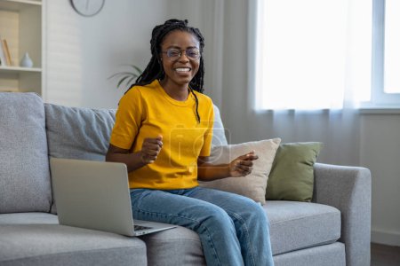 Téléchargez les photos : Jeune femme afro-américaine assise sur le canapé avec ordinateur portable - en image libre de droit