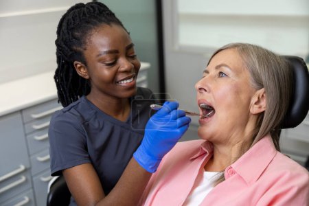 Patientin mittleren Alters sitzt im Zahnarztstuhl im medizinischen Zentrum, während ein Arzt ihre Zähne repariert