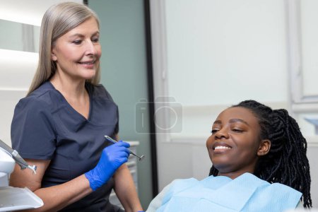 Téléchargez les photos : Une dentiste examine une patiente avec des outils en clinique dentaire qui reçoit un traitement dentaire en clinique - en image libre de droit