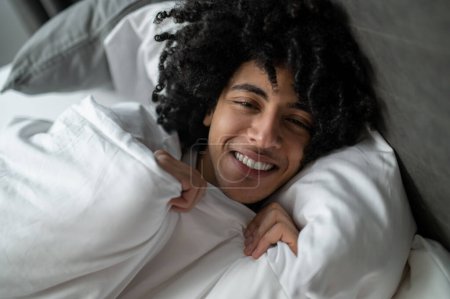 Early morning. Young brunette man lying in bed and looking sleepy