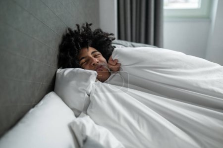 Early morning. Young brunette man lying in bed and looking sleepy