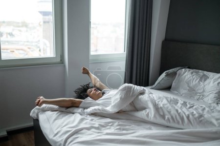 Stretching. Brunette young man lying in bed and stretching after sleep