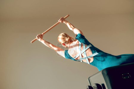 Téléchargez les photos : Jeune femme séduisante faisant de l'exercice d'étirement avec bâton d'exercice en bois au studio Pilates - en image libre de droit