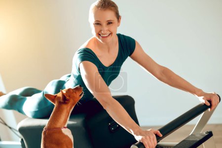 Téléchargez les photos : Femme blonde souriante faisant des exercices sportifs dans le studio Pilates avec son chien - en image libre de droit