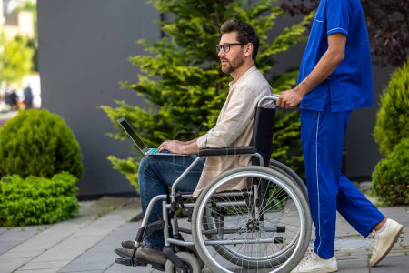 Téléchargez les photos : En promenade. Infirmière en uniforme bleu portant un fauteuil roulant avec patient masculin - en image libre de droit