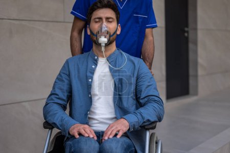 Téléchargez les photos : Dans un masque à oxygène. Jeune homme en fauteuil roulant portant un masque à oxygène - en image libre de droit