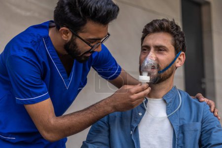 Téléchargez les photos : Soin. Homme infirmier portant un masque à oxygène sur un patient en fauteuil roulant - en image libre de droit