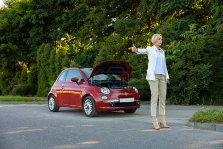 Foto de Mujer rubia de pie cerca de su coche roto y autoestop tener problemas con su auto en la carretera - Imagen libre de derechos