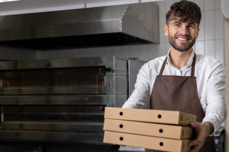 Photo for Handsome man in apron holding pizza boxes involving preparation and delivery of tasty Italian meals - Royalty Free Image