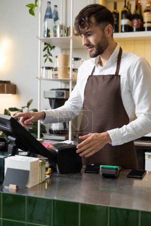Caucasian male barista at counter using cashbox computer in cafe store checking clients order