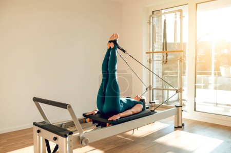 Téléchargez les photos : Entraîneur de fitness femme sportive démontre Pilates exercices sur simulateur profiter de routine active et athlétique - en image libre de droit