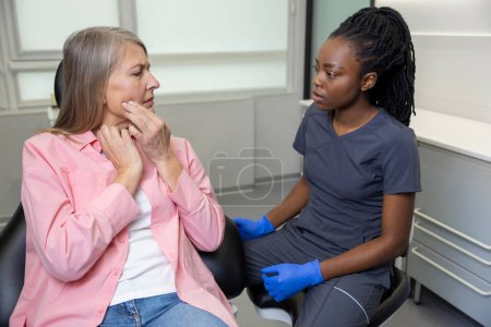 Téléchargez les photos : Une dentiste multiculturelle consulte une femme d'âge moyen dans une clinique de stomatologie - en image libre de droit