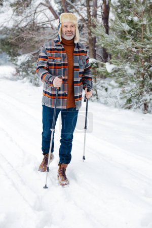 Foto de Actividad matutina. Hombre contento con palos escandinavos en un bosque nevado - Imagen libre de derechos