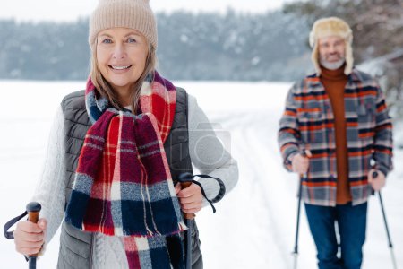 Photo for Winter fun. Happy mature couple with scandinavian stick on a walk in a forest - Royalty Free Image
