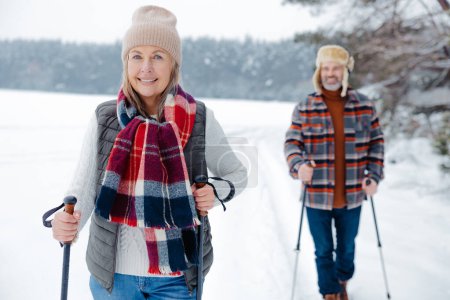 Téléchargez les photos : Amusement d'hiver. Heureux couple mature avec un bâton scandinave sur une promenade dans une forêt - en image libre de droit