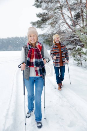Photo for Winter fun. Happy mature couple with scandinavian stick on a walk in a forest - Royalty Free Image