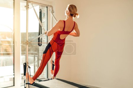 Foto de Atractiva mujer delgada entrenando su cuerpo deportivo en la máquina Pilates en el gimnasio - Imagen libre de derechos