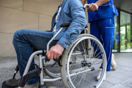 Foto de Incapacidad. Enfermera y un paciente discapacitado en el patio del hospital - Imagen libre de derechos