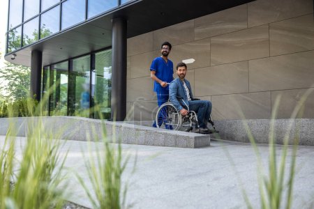 Foto de En una silla de ruedas. Paciente del hospital en silla de ruedas con un enfermero - Imagen libre de derechos