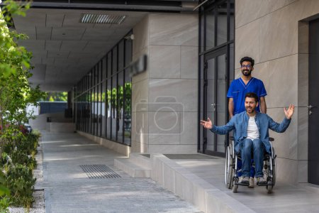 Foto de Paciente discapacitado. Enfermera morena llevando una silla de ruedas con un joven - Imagen libre de derechos