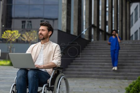 Téléchargez les photos : Homme avec ordinateur portable. Travailleur indépendant handicapé travaillant sur ordinateur portable assis en fauteuil roulant dans la cour de l'hôpital - en image libre de droit