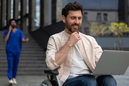 Téléchargez les photos : Homme avec ordinateur portable. Travailleur indépendant handicapé travaillant sur ordinateur portable assis en fauteuil roulant dans la cour de l'hôpital - en image libre de droit